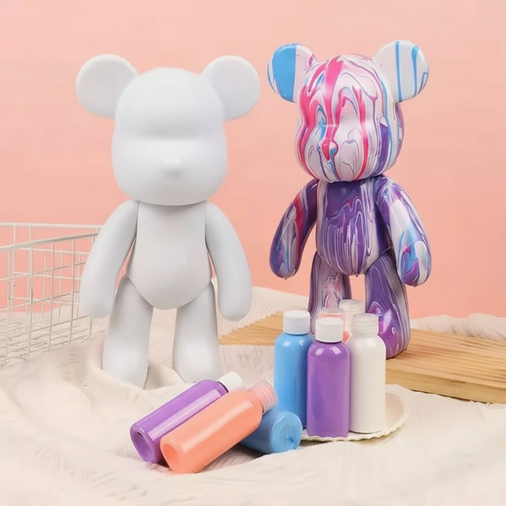 Two teddy bears, one white and one with colorful marbled design, surrounded by art supplies on a pink background.
